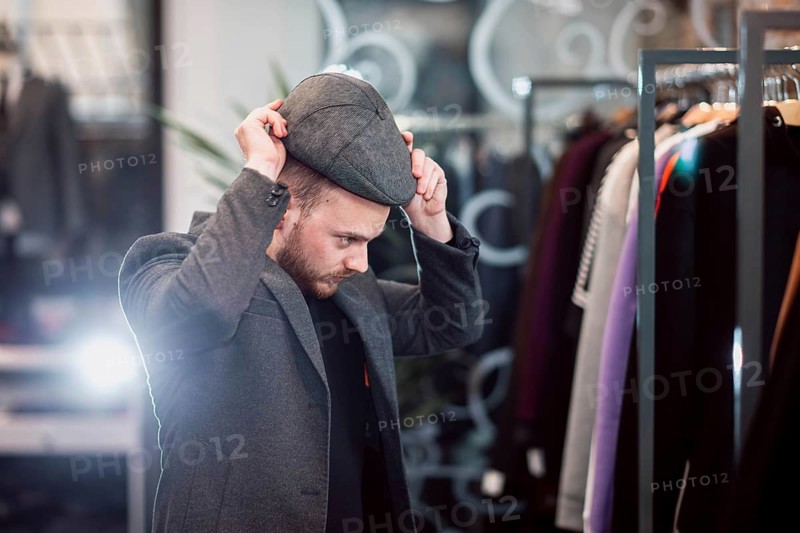 Individual trying on a flat cap in a fashionable clothing store setting