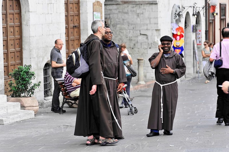 Group of monks in traditional robes on a busy city street, Assisi, Umbria, Italy