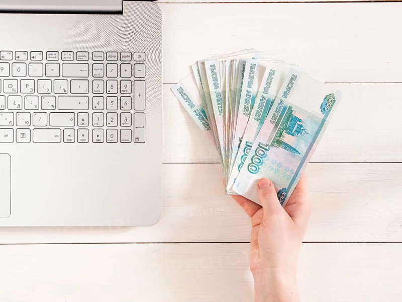 Hand holding russian rubles near laptop on white wooden background. Top view or flat lay. Finance and earning concept