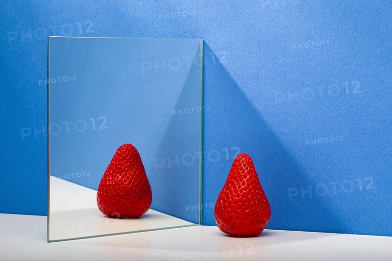 A fresh and tasty strawberry reflected in the mirror on the blue background. Fresh strawberry in the mirror reflection. Juicy strawberry