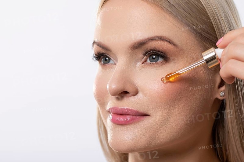 A woman gently applies a brightening serum to her face, promoting radiant and healthy skin with every touch