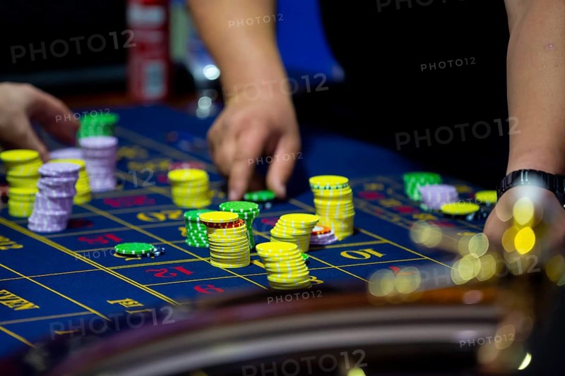 Roulette table with human hands putting down chips in casino. Roulette wheel in the foreground. Gamble game. Unrecognizable people