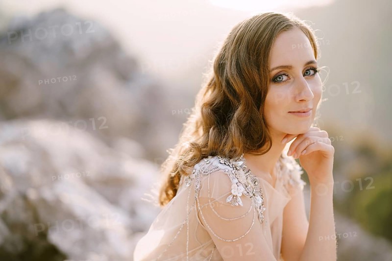 Smiling bride sits with her head propped up with her hand. Close-up.