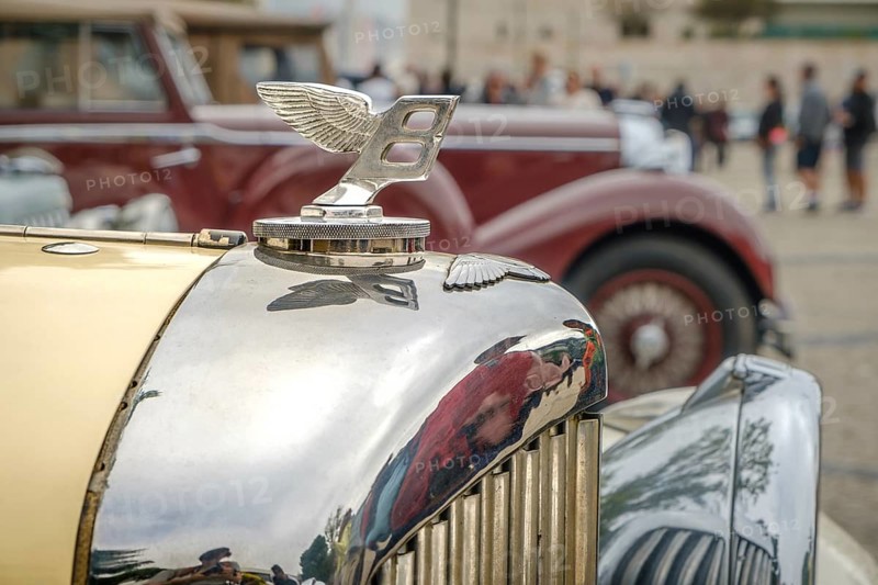 Lisbon, Portugal - Oct 15, 2023: Close-up and selective focus on the Bentley Wings Flying B mascot hood ornament or bonnet badge of 1930s against other car background