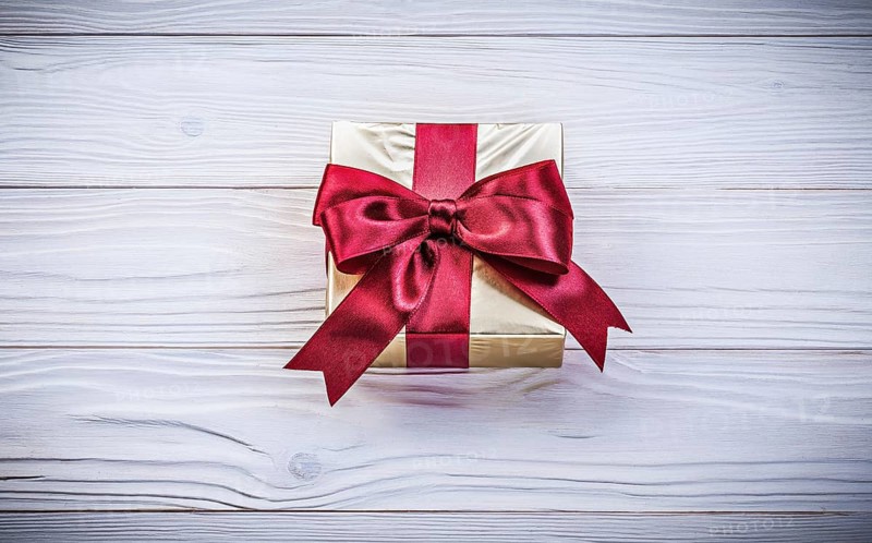 Golden gift-container with tied bow on wood board holidays concept