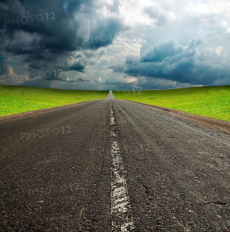 Old broken asphault road in green field over blue cloudy sky
