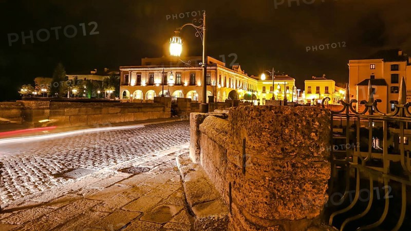 Night time on the historic landmark New Bridge Puente Nuevo of Ronda town in Spain. with running cars across the road and moving people and cars