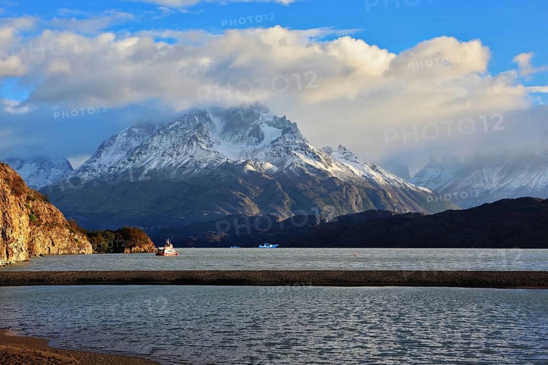 Gray lake and snow-capped mountains. By the banks of the red tourist ship sails. Summer sunset illuminates the lake. National Park Torres del Paine, Chile