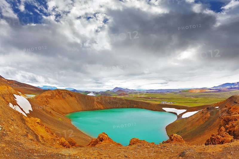 Summer in Iceland. Picturesque lake in the crater of an extinct volcano. Lake water bright green color. On the shores lie snowfields from last year