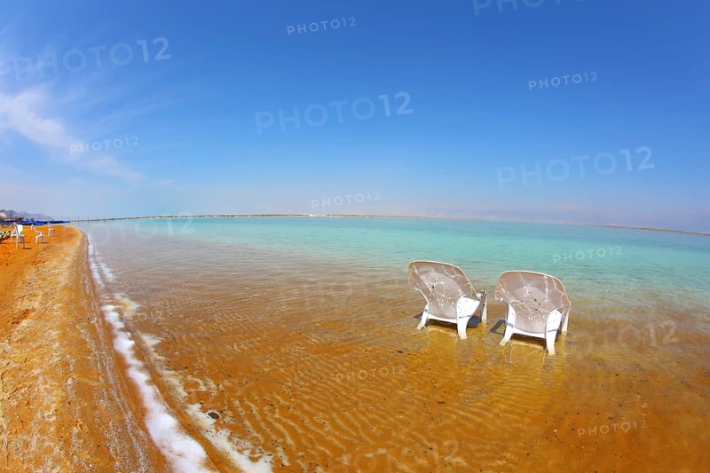 Two white beach armchairs stood side by side in the water at the beach. Dead Sea, Israel