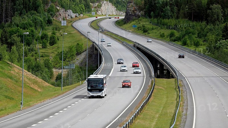 Summer motorway landscape with white Iveco Evadys tour bus among car traffic. Salo, Finland, June 30, 2018