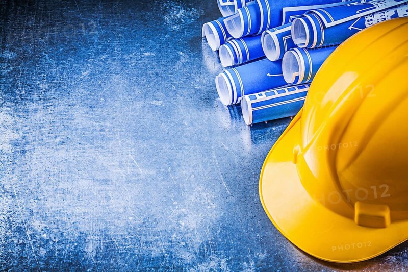 Blue engineering drawings yellow hard hat on scratched metallic background construction concept