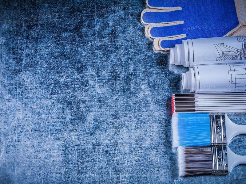 Copyspace of wooden meter paintbrushes protective gloves and rolled blueprints