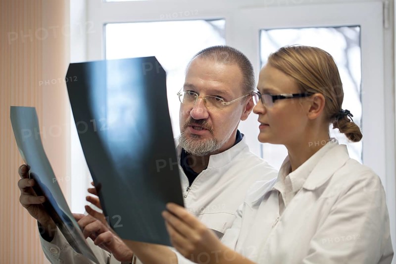 Senior and young doctors analyzing and dicussing the result of x-ray examination. They having two images to compare