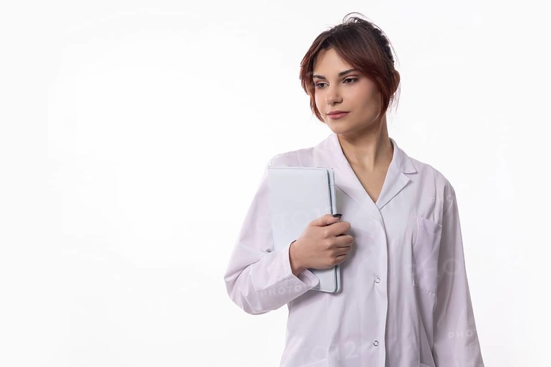A confident female healthcare professional dressed in a crisp white coat is thoughtfully holding a tablet