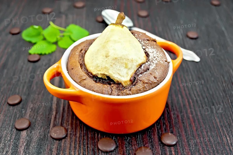 Cake with chocolate and pear in red roaster, mint and spoon on a background of dark wood planks