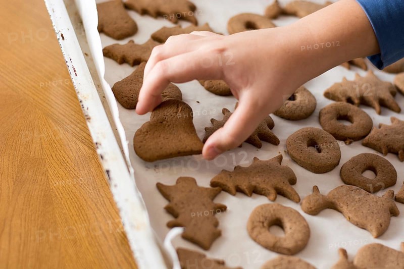 Boy picking up baked gingerbread cookie from a white plate