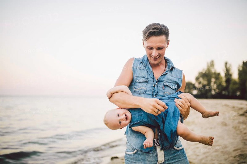 Theme Fatherhood and rest with a child at sea. Young handsome Caucasian father plays plays enjoys throwing up in arms his child up in summer daughter on the sandy beach on the seashore