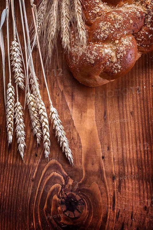 Loaf of breead and wheat ears on vintage wooden board with small copyspace food and drink concept