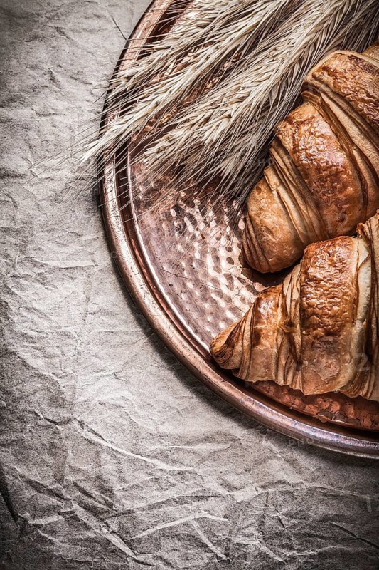 Golden wheat rye ears fresh croissants copper tray on wrapping paper