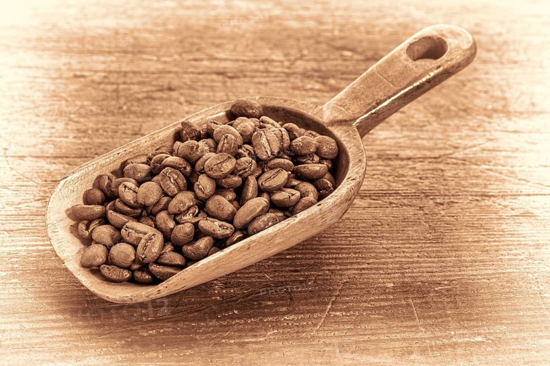 Rustic scoop of roasted coffee beans against a grunge painted wood background, retro sepia toning
