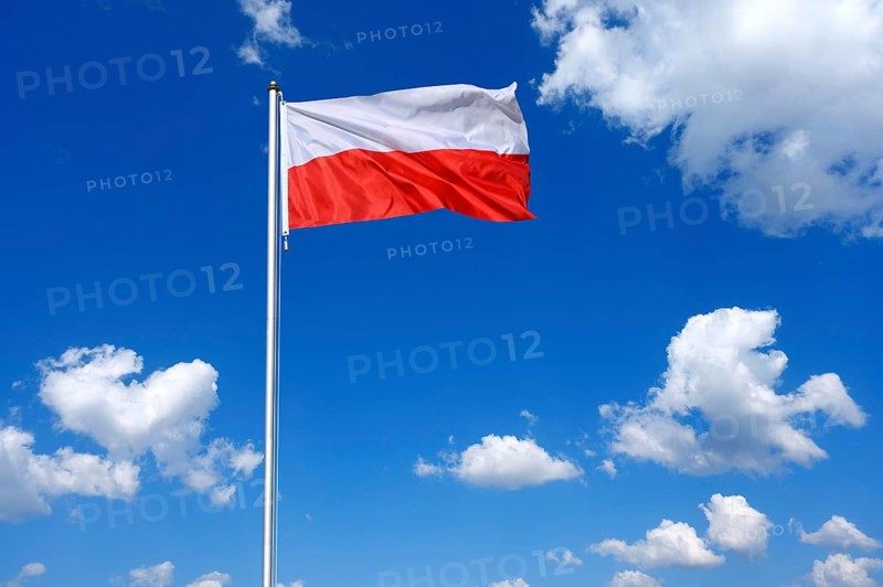 The flag of Poland flutters in the wind in a blue sky with white clouds