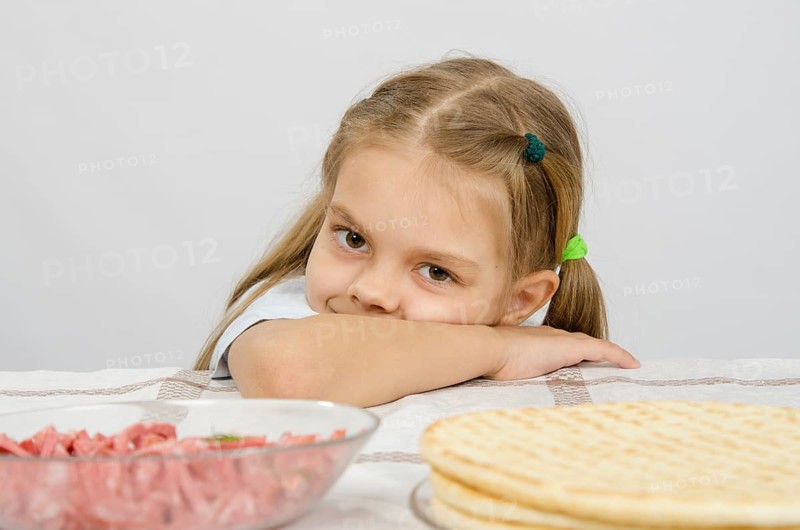 Little girl sitting at a table with his head on his hand with a smile and looking at the food in front of her