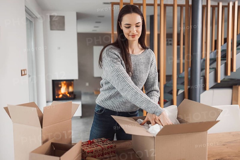 Young caucasian woman wrapping a gift, getting it ready to send in the post. Woman packaging a surprise gift for a family member, packaging it into a brown cardboard box