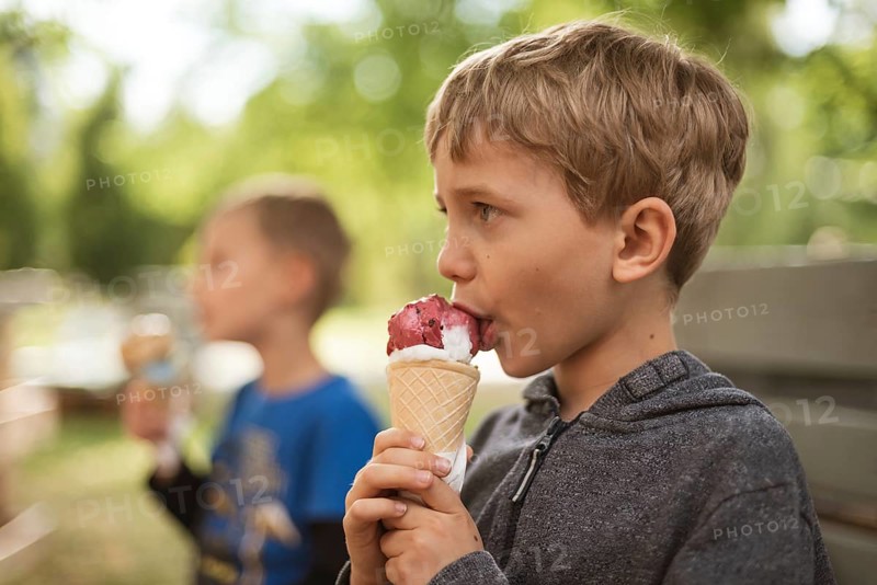 Two young boys eats ice cream in the park