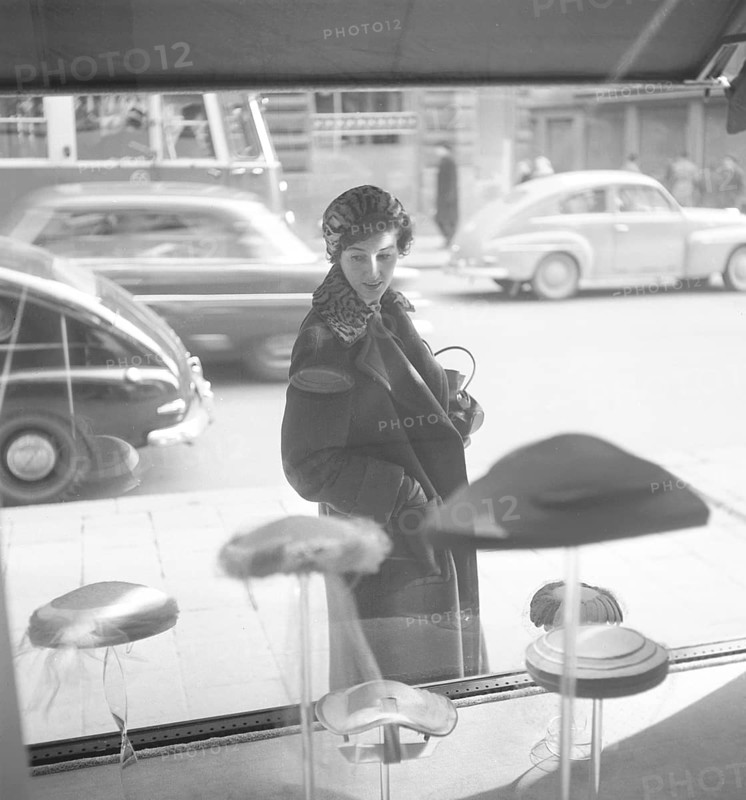 Window shopping in the 1950s. A woman is standing outside a boutique with the latest fashion in hats in their display window. Sweden 1955. Photo Kristoffersson BS46-7