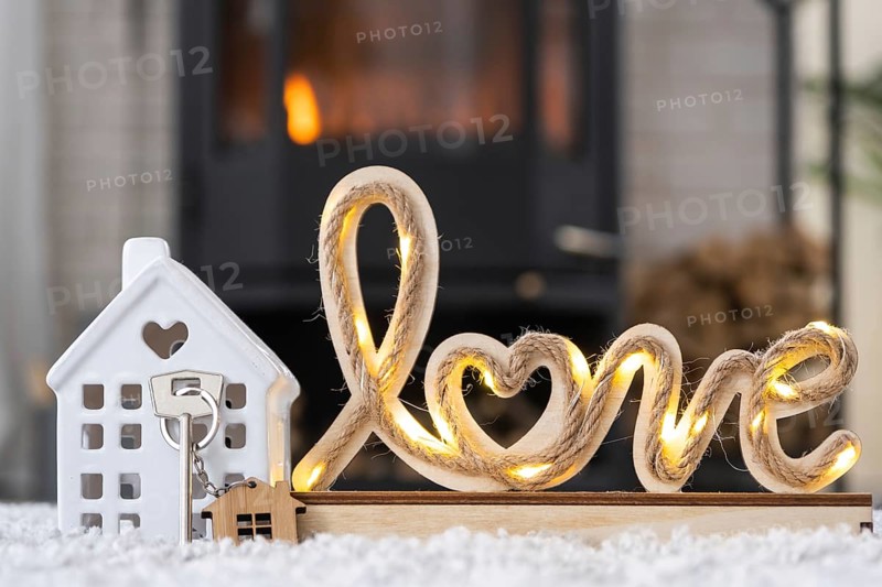 Key to house with keychain against background of fireplace stove with fire and firewood in Valentine decor, love home. Moving to new house, mortgage, rent and purchase real estate