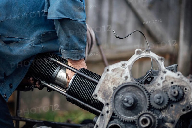 A person working on an engine outdoors, focusing on metal and mechanical components