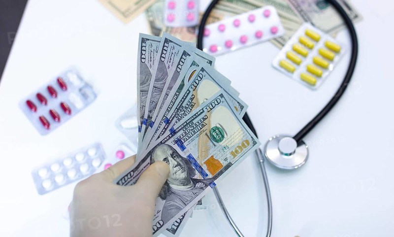 Hand with cash, stethoscope, and pills, illustrating high cost of healthcare