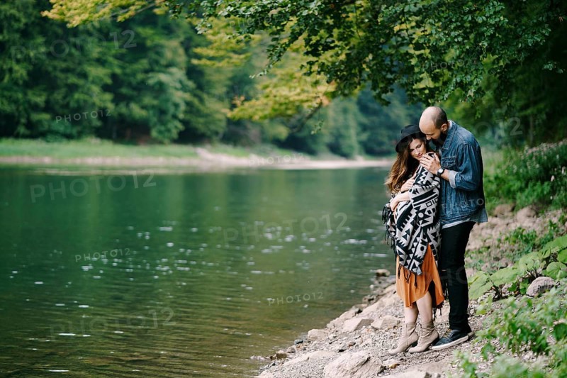 Man hugs a pregnant woman by the lake.
