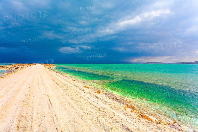 Low winter clouds are reflected in the green sea water. The landfill embankment runs through the sea. Winter thunderstorm begins. Israel. The picturesque Dead Sea