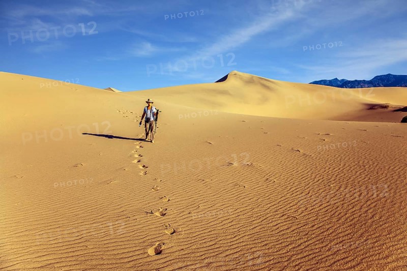 Woman with a camera and a tripod goes among the dunes. USA. Mesquite Flat Sand Dunes, Death Valley, California. Light sand waves from the desert wind. Concept of active and photo tourism