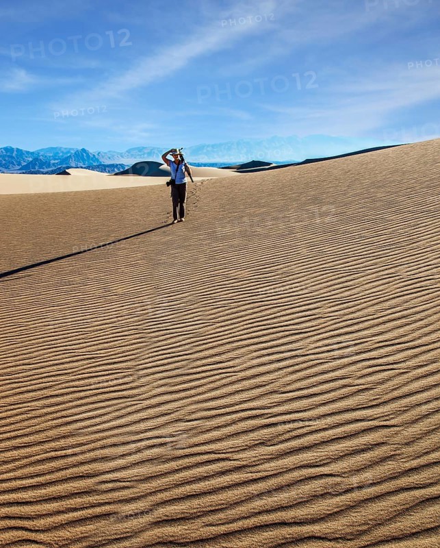 USA. Mesquite Flat Sand Dunes, Death Valley, California. Woman with a camera and a tripod goes among the dunes. Light sand waves from the desert wind. Concept of active and photo tourism