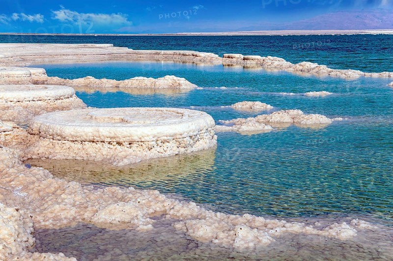 The evaporated salt forms bizarre crystal shapes on the surface of the water. Israeli coast, warm winter February day. Unique Dead Sea. The drainless salt lake in the Middle East