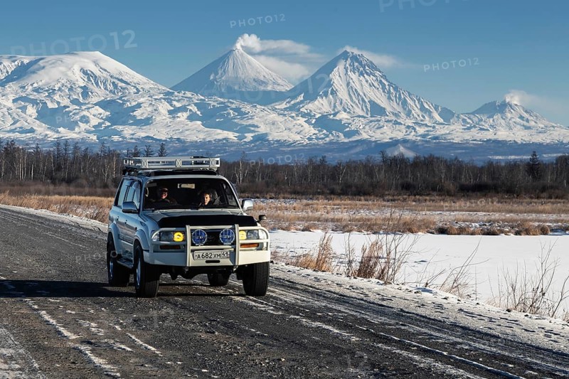 Japanese Sport Utility Vehicle Toyota Land Cruiser driving along road on background beautiful winter landscape, active Kluchevskoy Volcano on sunny day. Kamchatka Peninsula, Russia, January 7, 2016