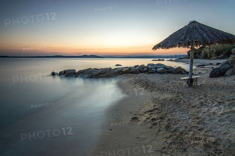 View through rocks on a sandy beach into the sunset. Landscape shot with view to the horizon over the wide sea at the coast of Ouranoupoli, Thessaloniki, Central Macedonia, Greece
