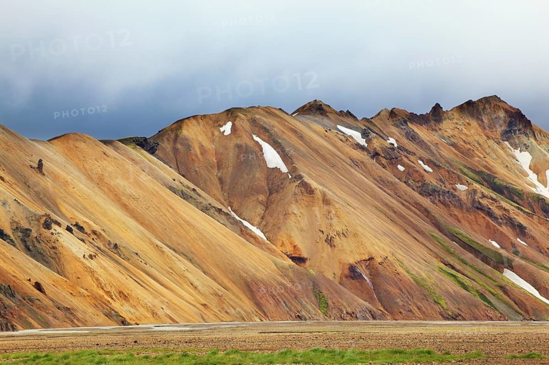 Smooth orange rhyolite mountains in Landmannalaugar nature reserve. In the hollows snow left over from last year