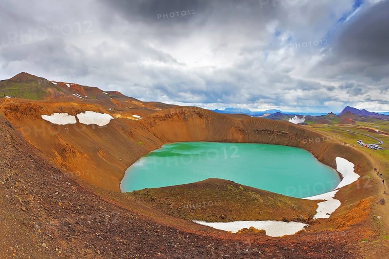 July in Iceland. Lake in the crater of an extinct volcano. Lake water bright green color. On the shores lie snowfields from last year