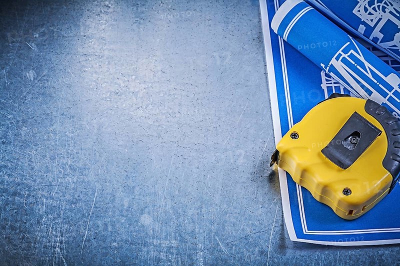 Assortment of blue construction plans measuring tape on metallic background