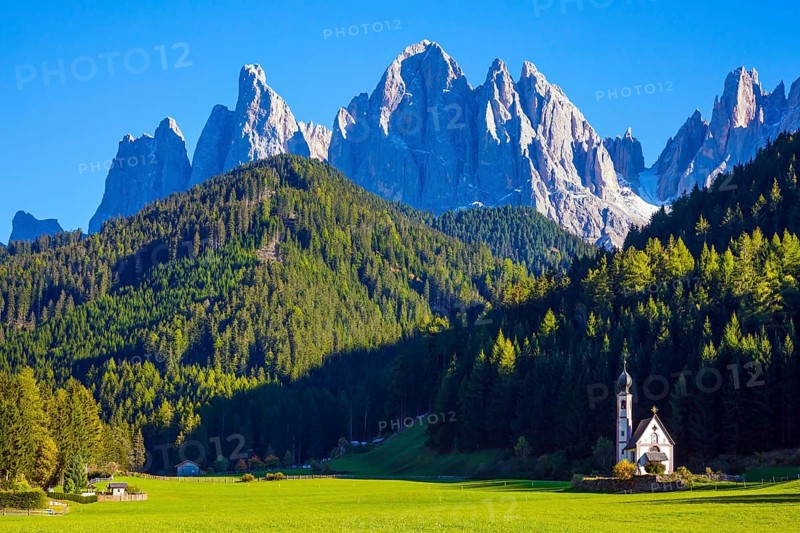 Small white church with among green lawns on the sunset. The village Santa Maddalena in the Val di Funes Valley. Italy, Tyrol. The concept of active, ecological and photo tourism