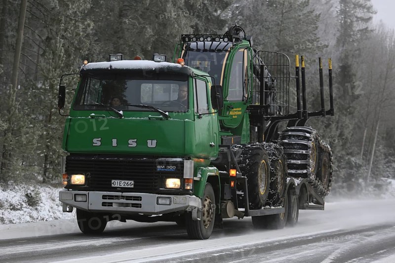 SALO, FINLAND, JANUARY 8, 2017: Green SISU SM300 truck transports a John Deere Forestry forwarder along snowy highway flanked by forest on a cold winter afternoon in South of Finland