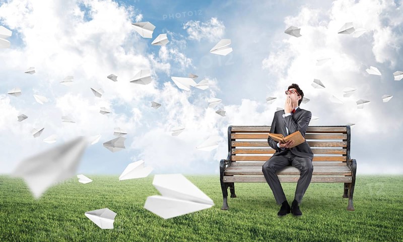Young student with a book on the bench. traditional learning concept. paper planes fly around
