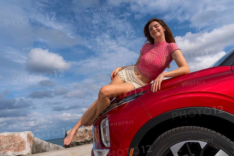 A gorgeous redhead model sits confidently on the hood of her car, soaking in the summer breeze as she embarks on an exciting cross-country adventure, the open road stretching ahead with endless possibilities, Milwaukee, United States of America