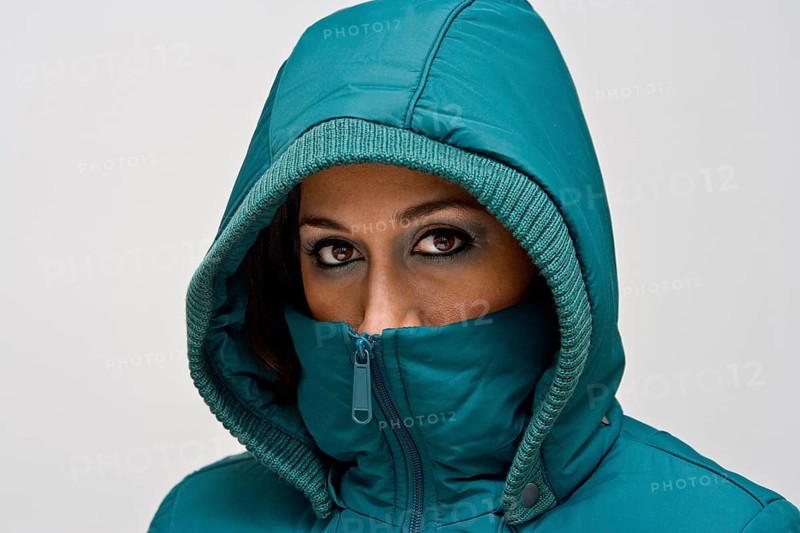 A young woman wearing a green winter coat using the hood to cover her head so that only her eyes are visible, isolated on white, New York, USA