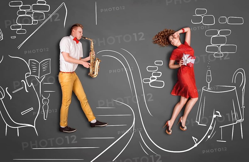 Love story concept of a romantic couple against chalk drawings background. Male playing the saxophone in a restaurant for his girlfriend