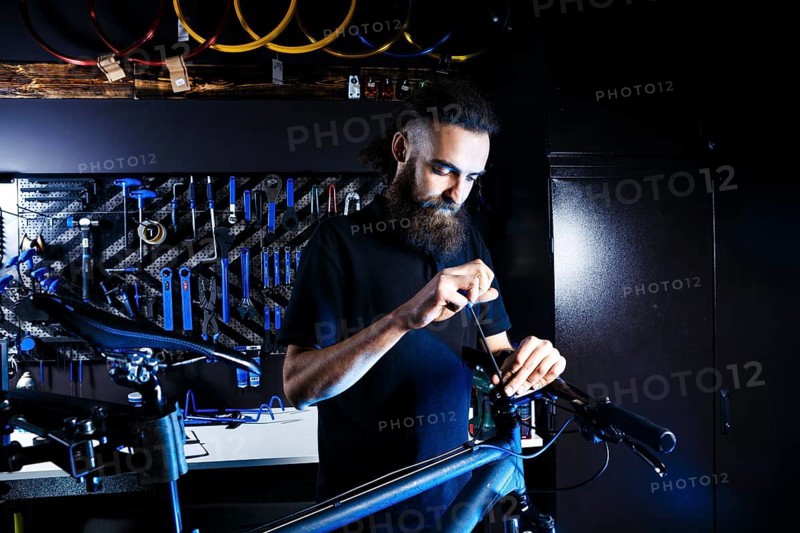 Theme sale and repair of bicycles. Young and stylish with a beard and long hair, a Caucasian man uses a tool to set up and repair a bike in a store. Business owner at work